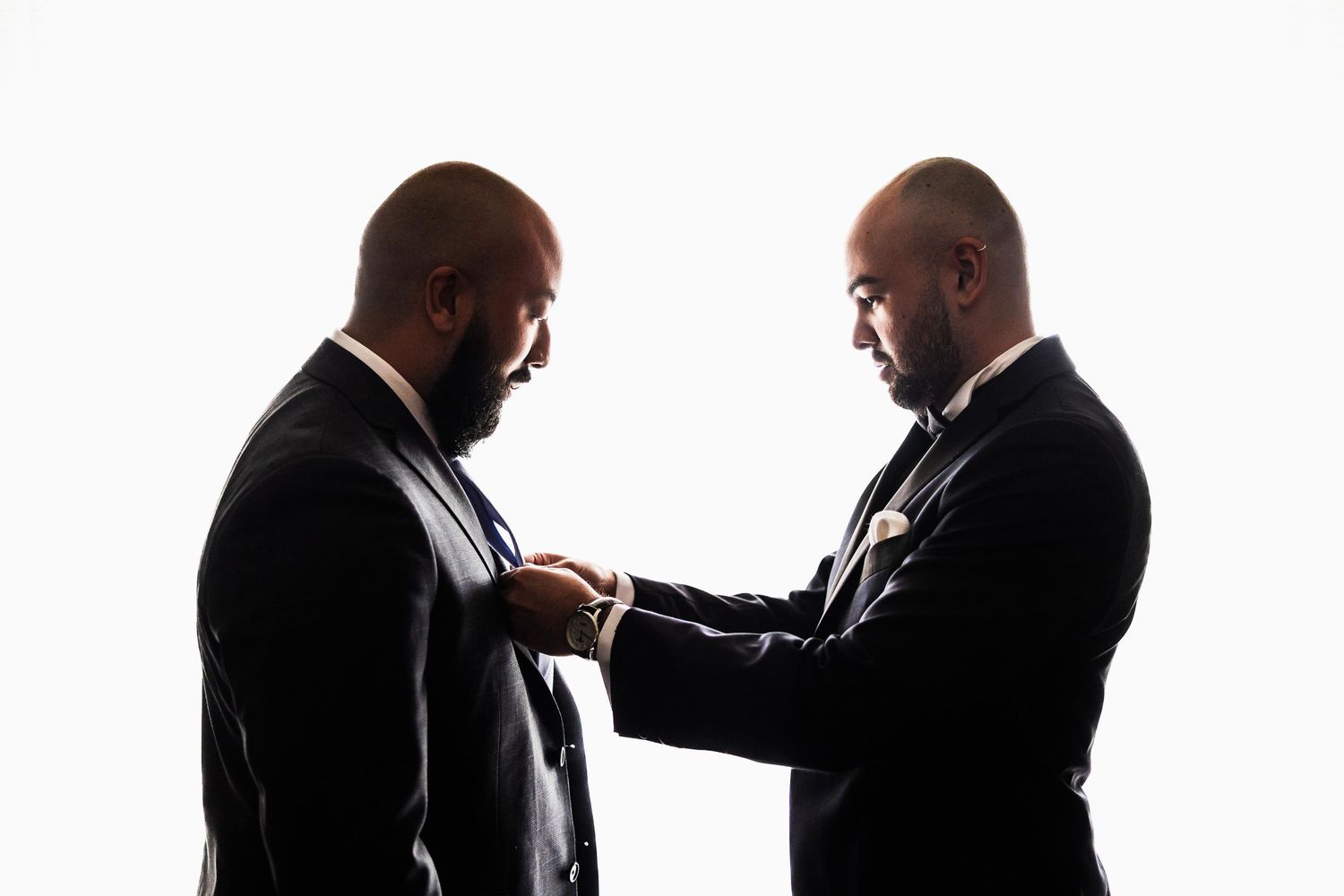 A silhouetted image of two men in suits adjusting formal attire.