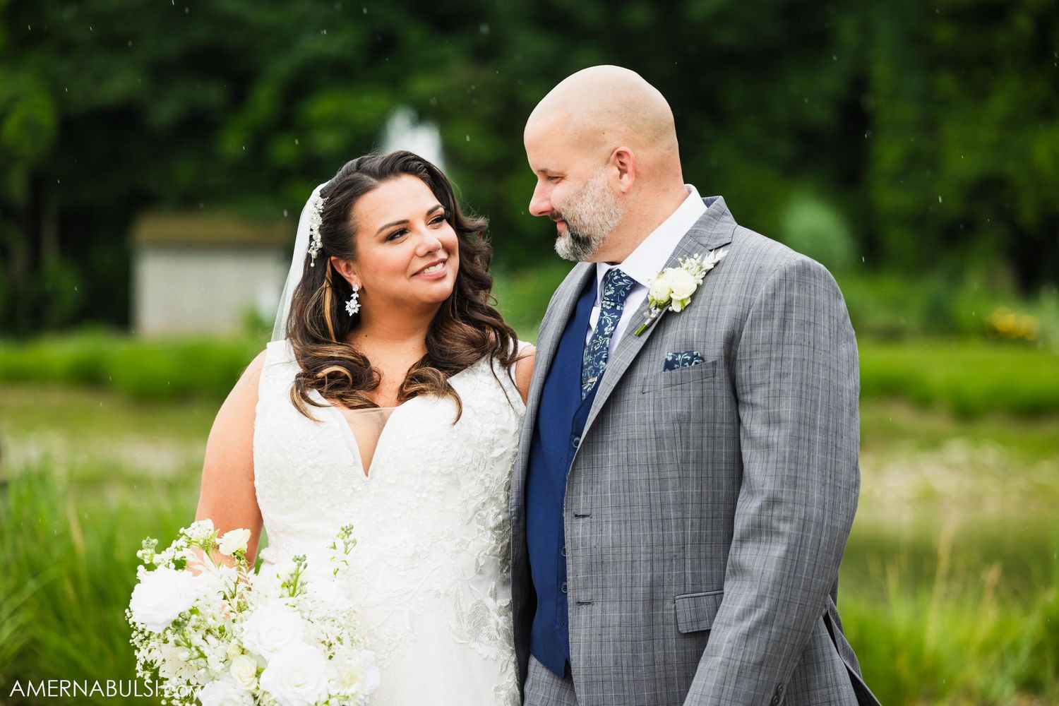 Newlyweds pose together outdoors in formal wedding attire.