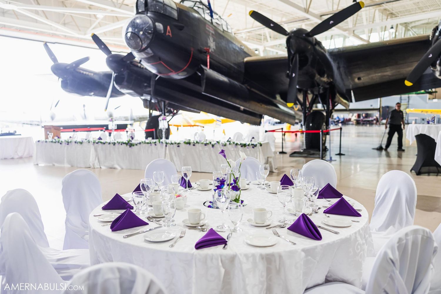 Elegant wedding reception tables set beneath vintage aircraft displays in an aviation museum.