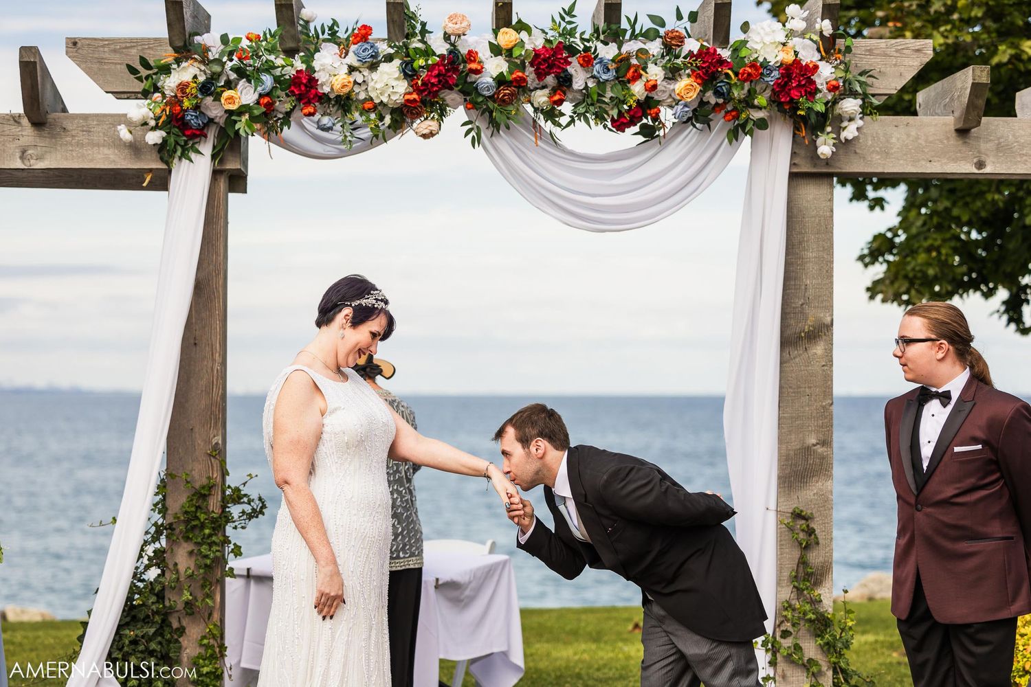 Playful moment during outdoor wedding ceremony under floral decorated arch with ocean backdrop.