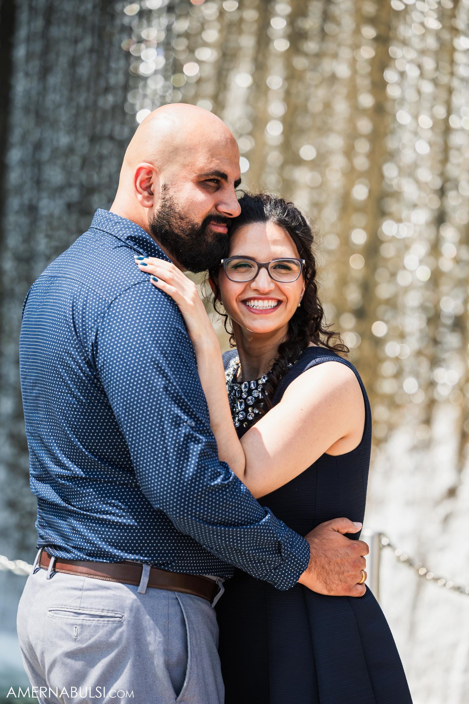 A romantic couple embraces in front of a sparkly backdrop during an engagement photo shoot.
