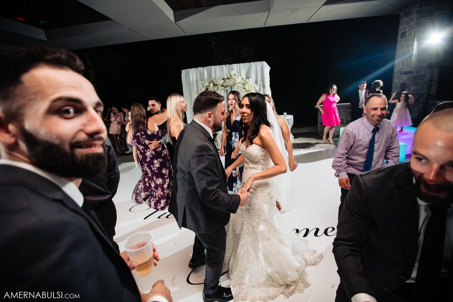 Wedding reception dance floor filled with guests celebrating in evening lighting.