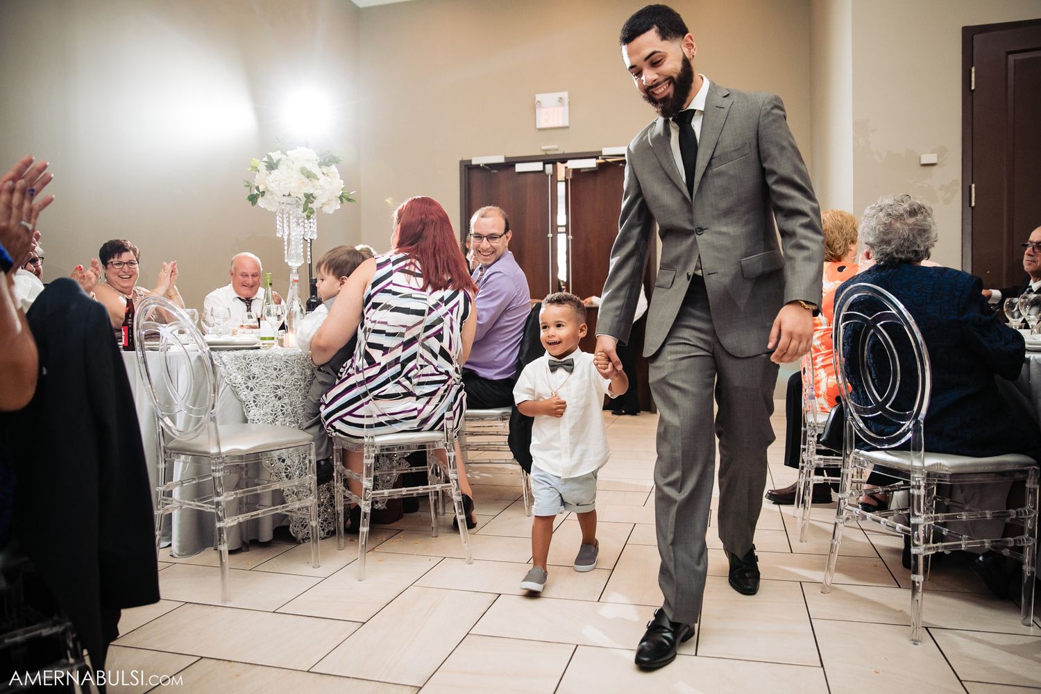 Wedding guests celebrating while a child runs across the dance floor at a reception.