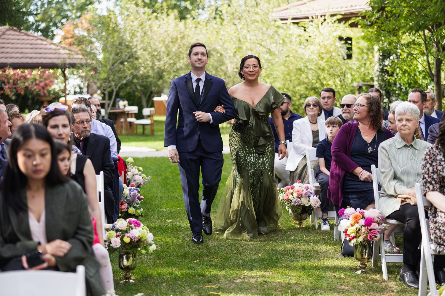 Couple walks down the aisle together at an outdoor garden wedding ceremony with seated guests.