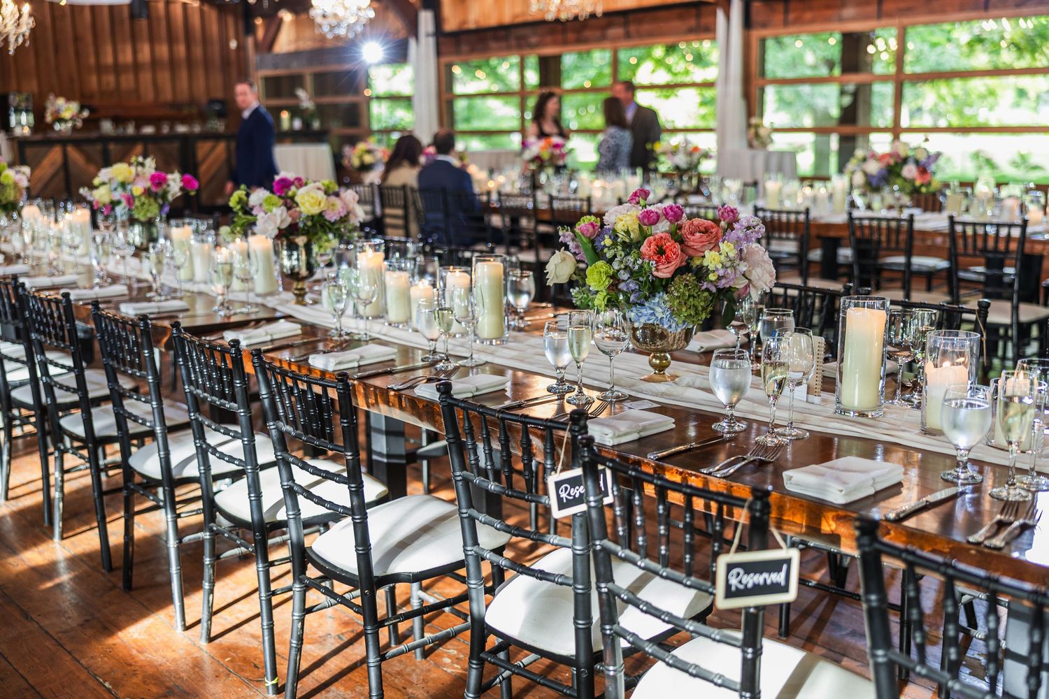 Rustic barn wedding reception with long tables, black chiavari chairs, floral centerpieces, and reserved bride and groom signs.