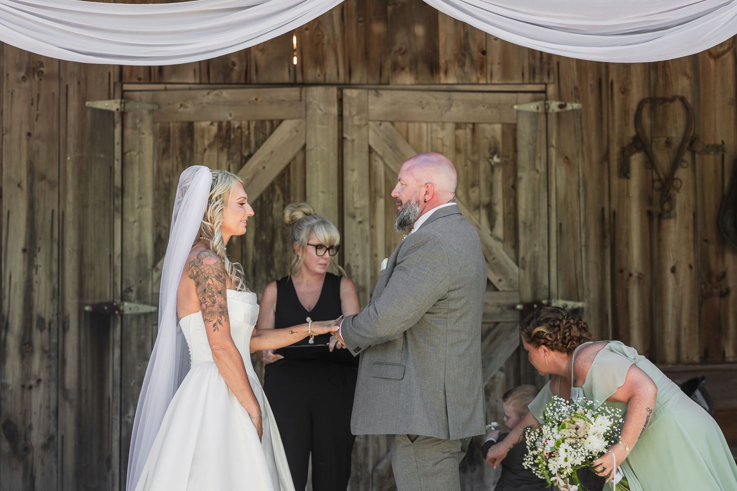 Bride and groom exchange vows before officiant at rustic barn wedding ceremony.