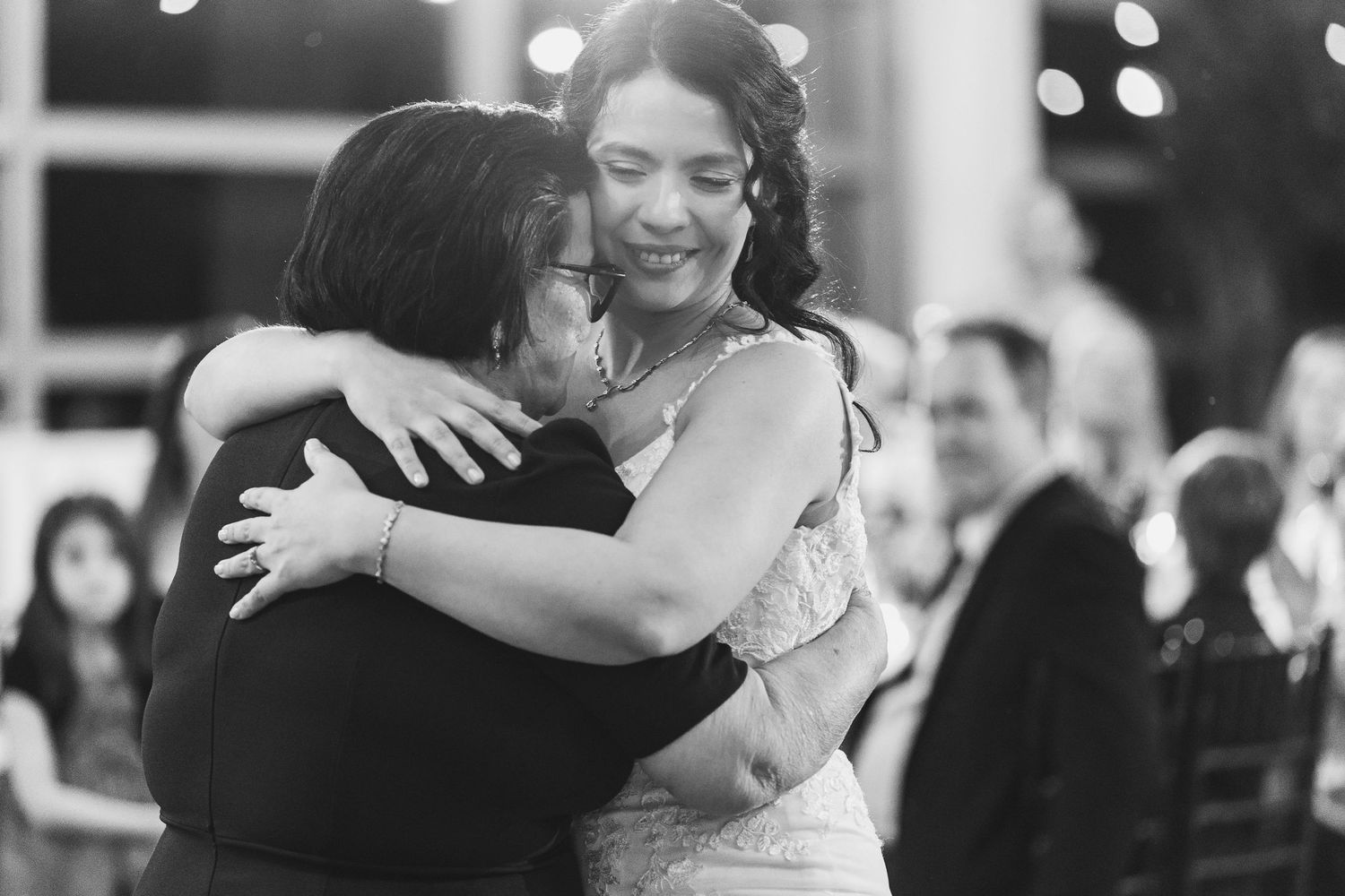 Bride shares an emotional hug with a guest during a wedding reception in black and white photo.