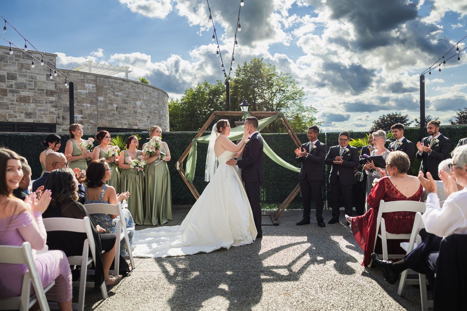 Bride and groom kiss at outdoor wedding ceremony as guests celebrate with ribbon streamers.