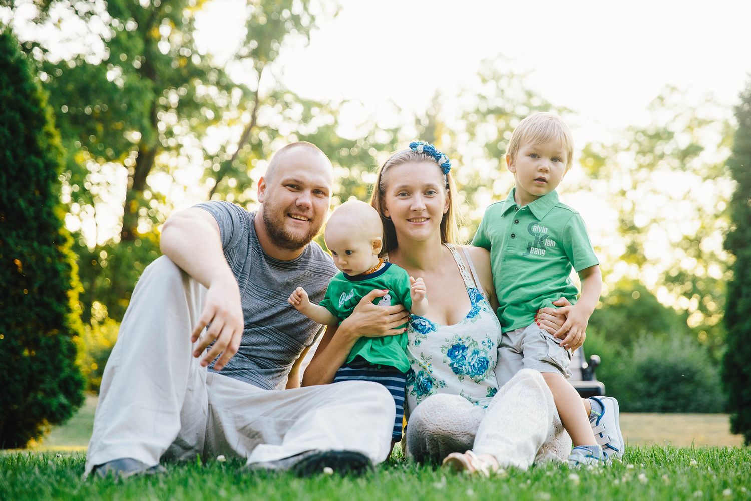 Family enjoying a playful outdoor photo session in a sunlit park setting with natural greenery.