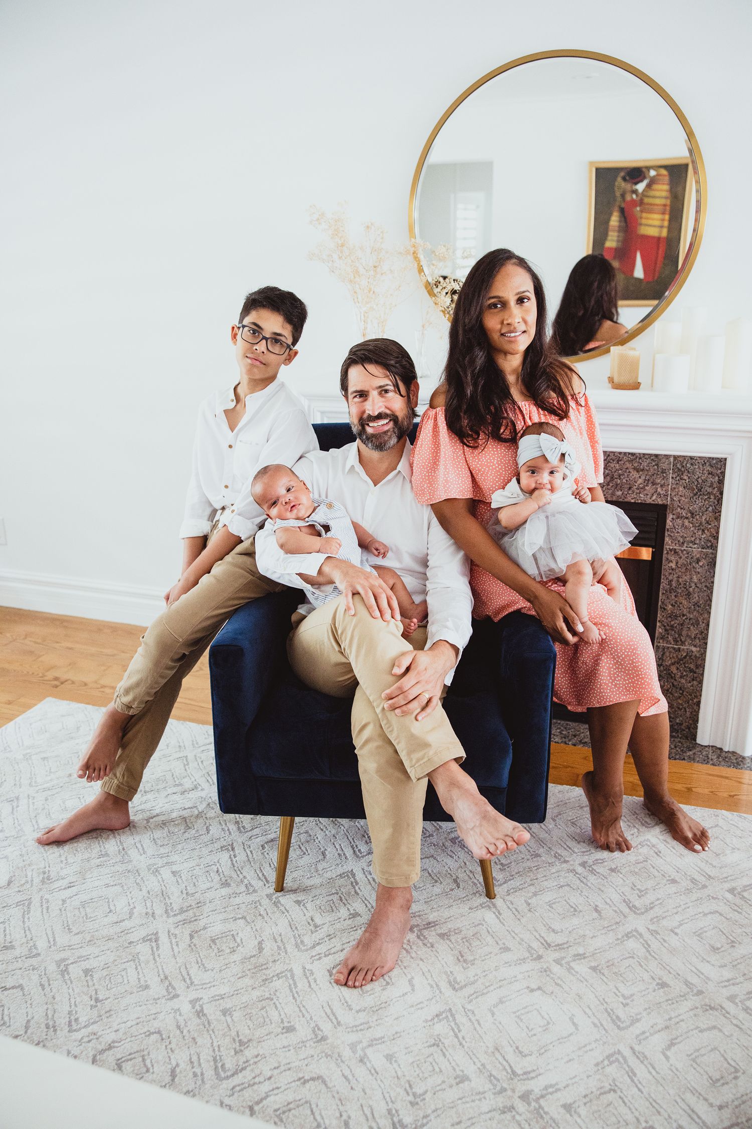 Family sitting and playing together on a patterned gray rug in a bright white living room.