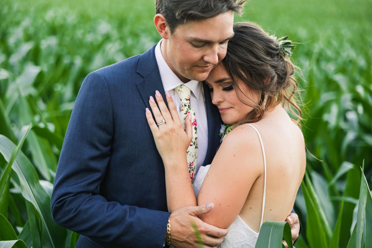 Romantic couple embraces in a lush green cornfield setting.