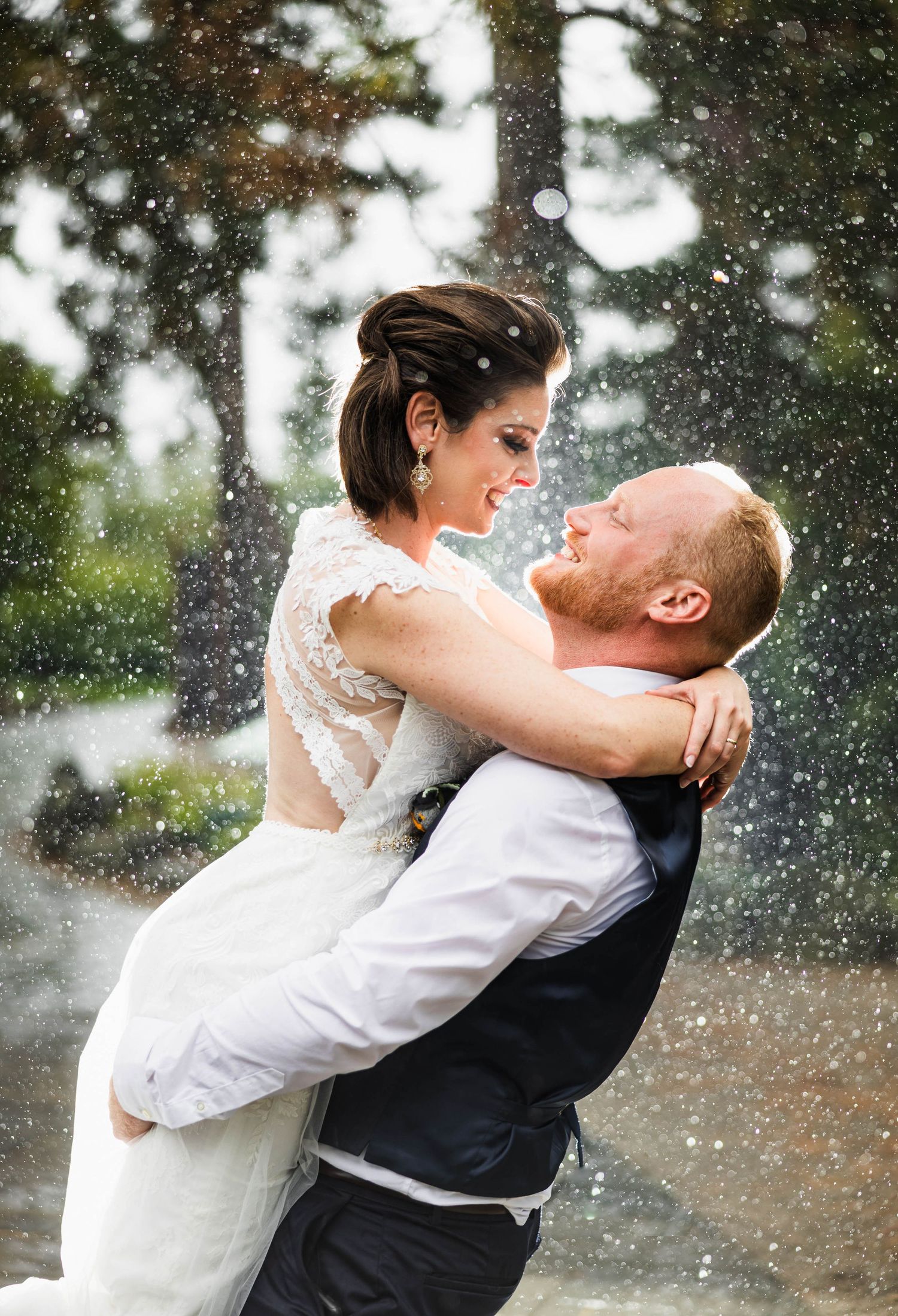 A romantic wedding couple embraces in the falling snow during an outdoor photoshoot.