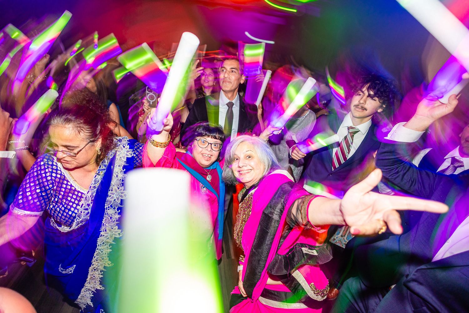 Energetic crowd dancing with glowing neon light sticks at a nightclub party with colorful purple lighting effects.
