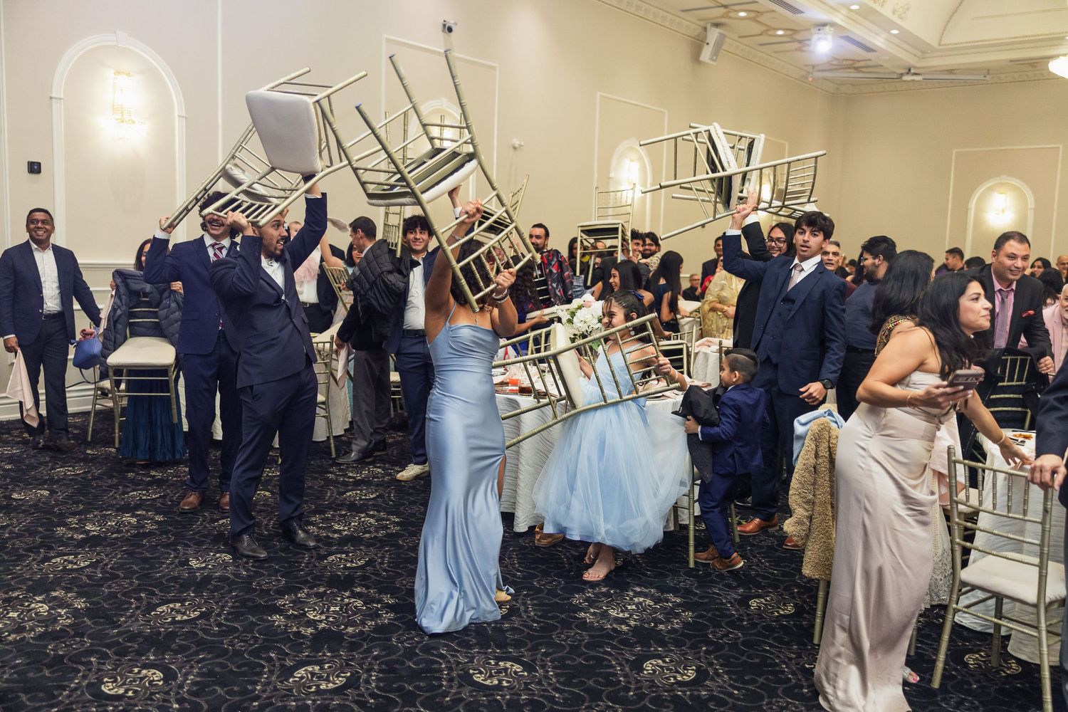 Wedding reception guests dance in a circle with their arms linked together on a dance floor.