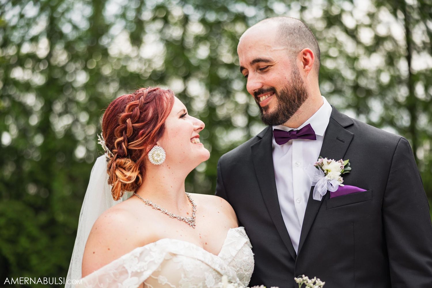 A joyful wedding couple shares a candid moment outdoors with green foliage in the background.