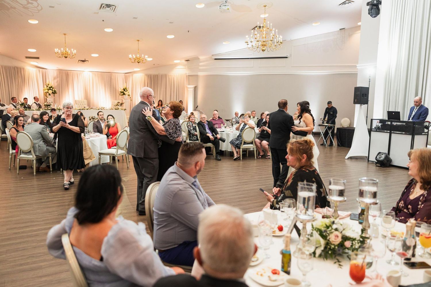 Wedding reception venue with guests dining at decorated tables under crystal chandeliers.