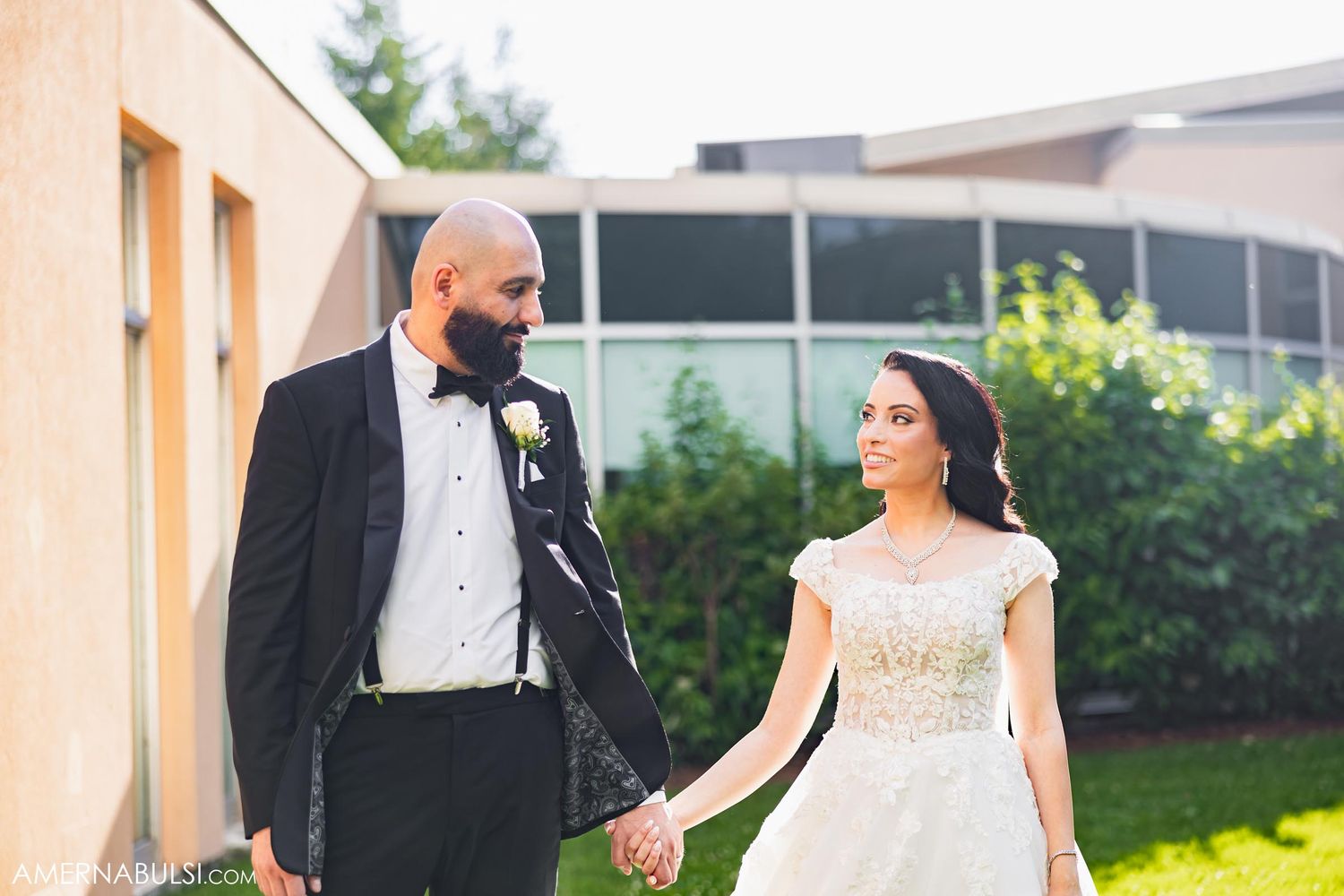 Newlyweds walk hand in hand outside on their wedding day in formal attire.