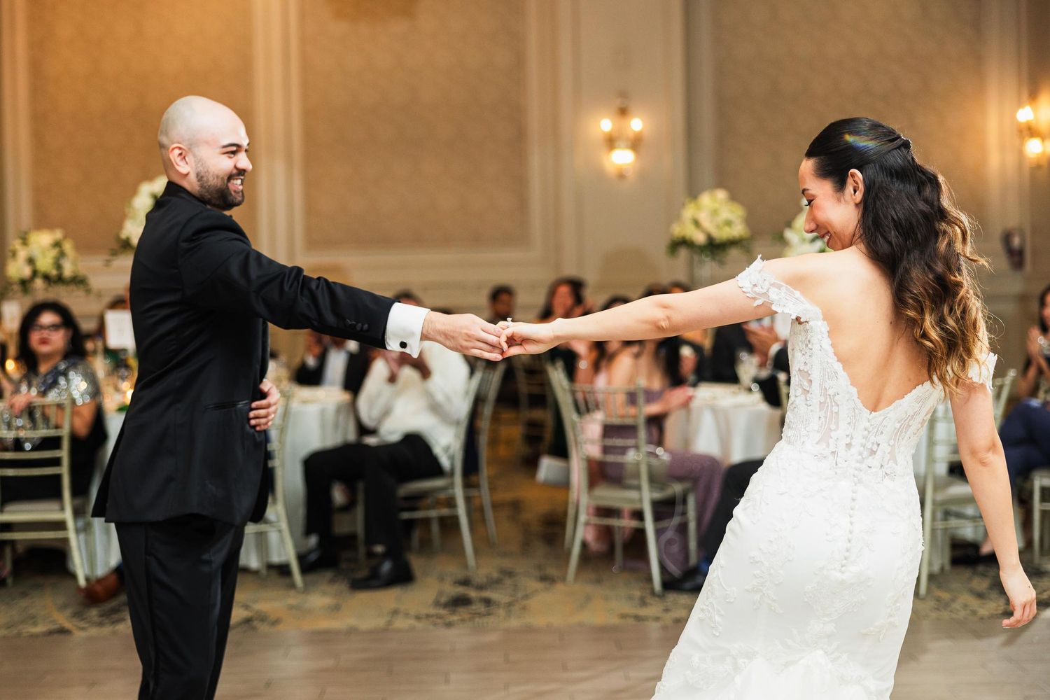 A couple dances energetically in a beautifully lit ballroom during their wedding reception.