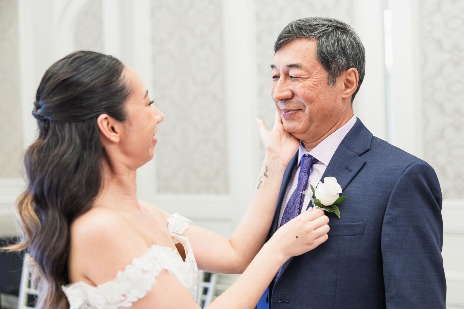 Emotional wedding moment captured between two people in formal attire against light background.