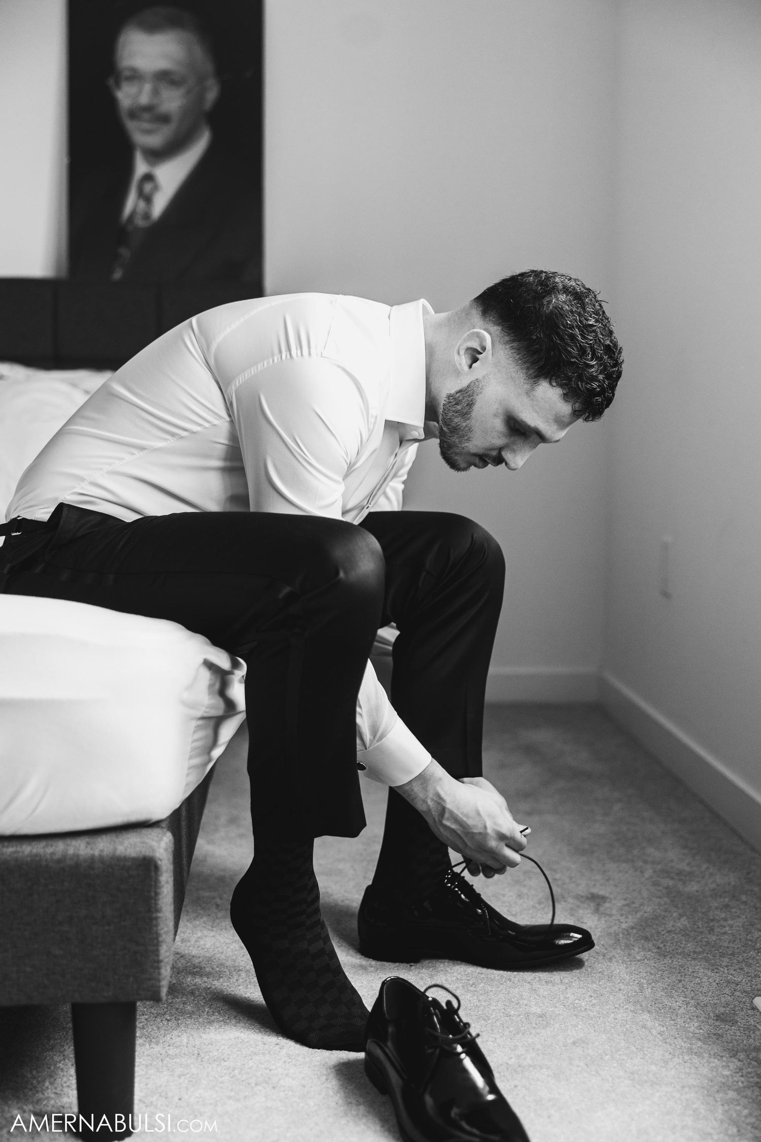Person in white shirt sitting on sofa putting on formal black dress shoes.