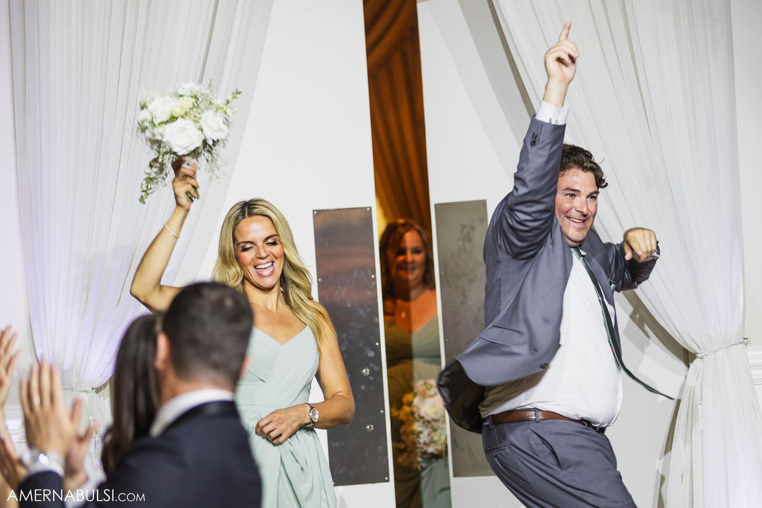 Wedding party members celebrate with raised arms and bouquets during reception entrance.