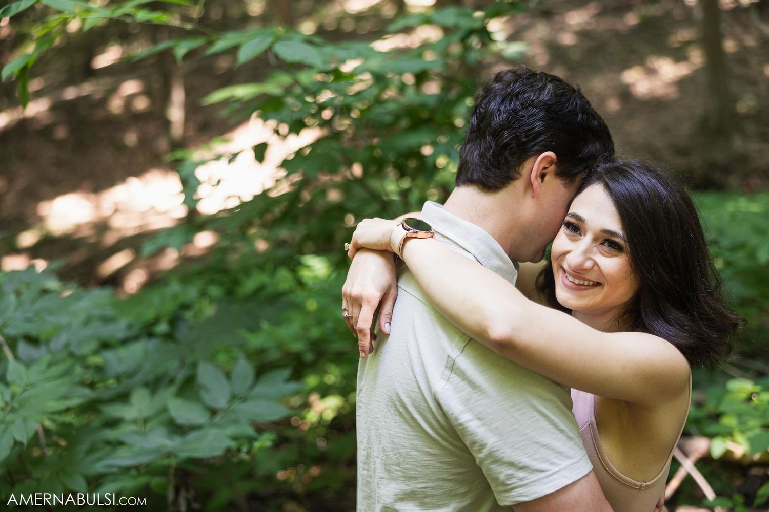 Couple sharing joyful embrace in dappled forest sunlight.