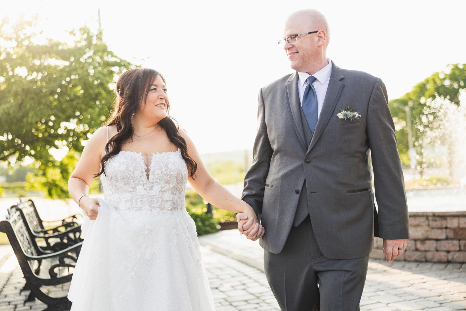 A wedding couple walking together on a sunny patio with benches in the background.
