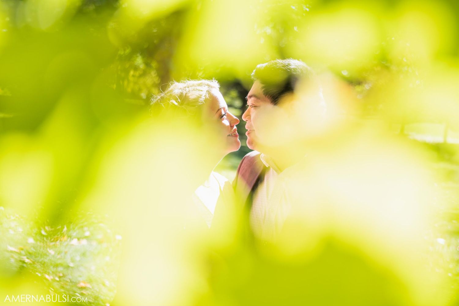 Soft focus romantic kiss framed by blurred green foliage.