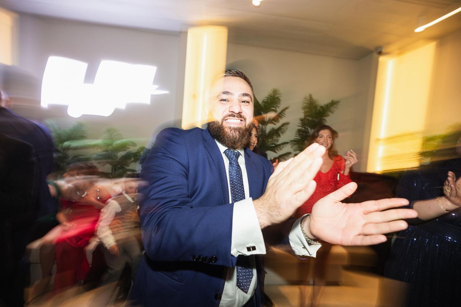 A guest in a navy suit claps enthusiastically during a lively celebration moment.
