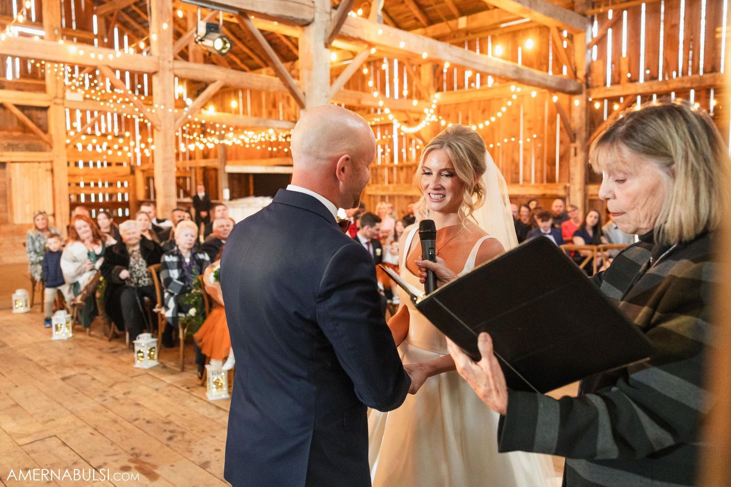 Wedding ceremony in warmly lit barn with wooden beams and rustic details.