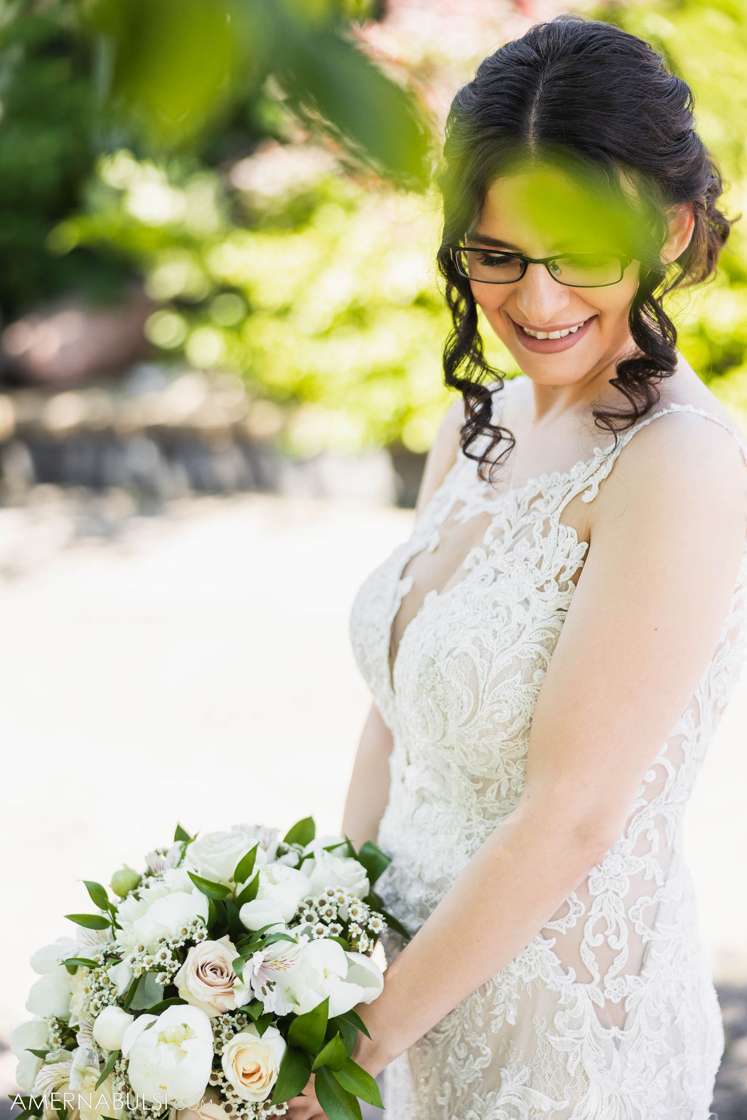 Sunlit bridal portrait through garden foliage with white and pink bouquet.