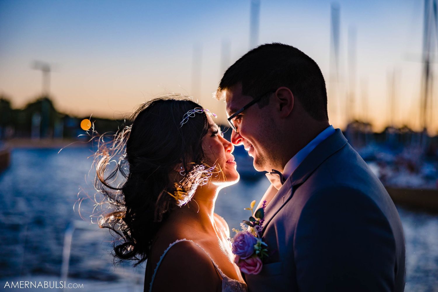 Backlit couple shares intimate moment at marina during golden hour.