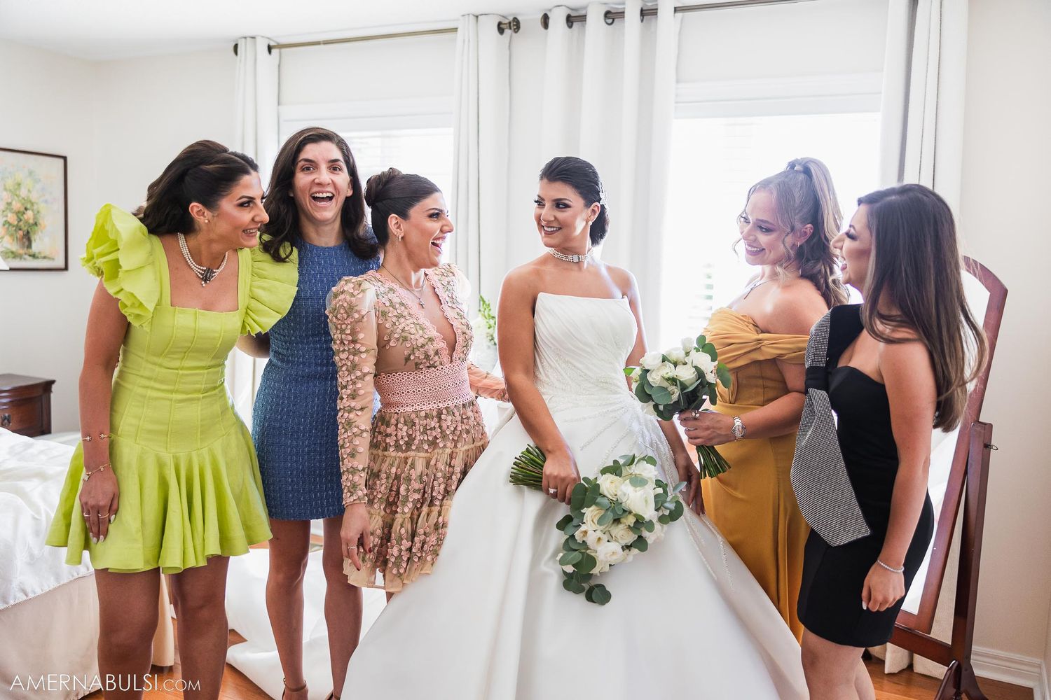 Wedding party in colorful dresses gathers around bride in white gown.