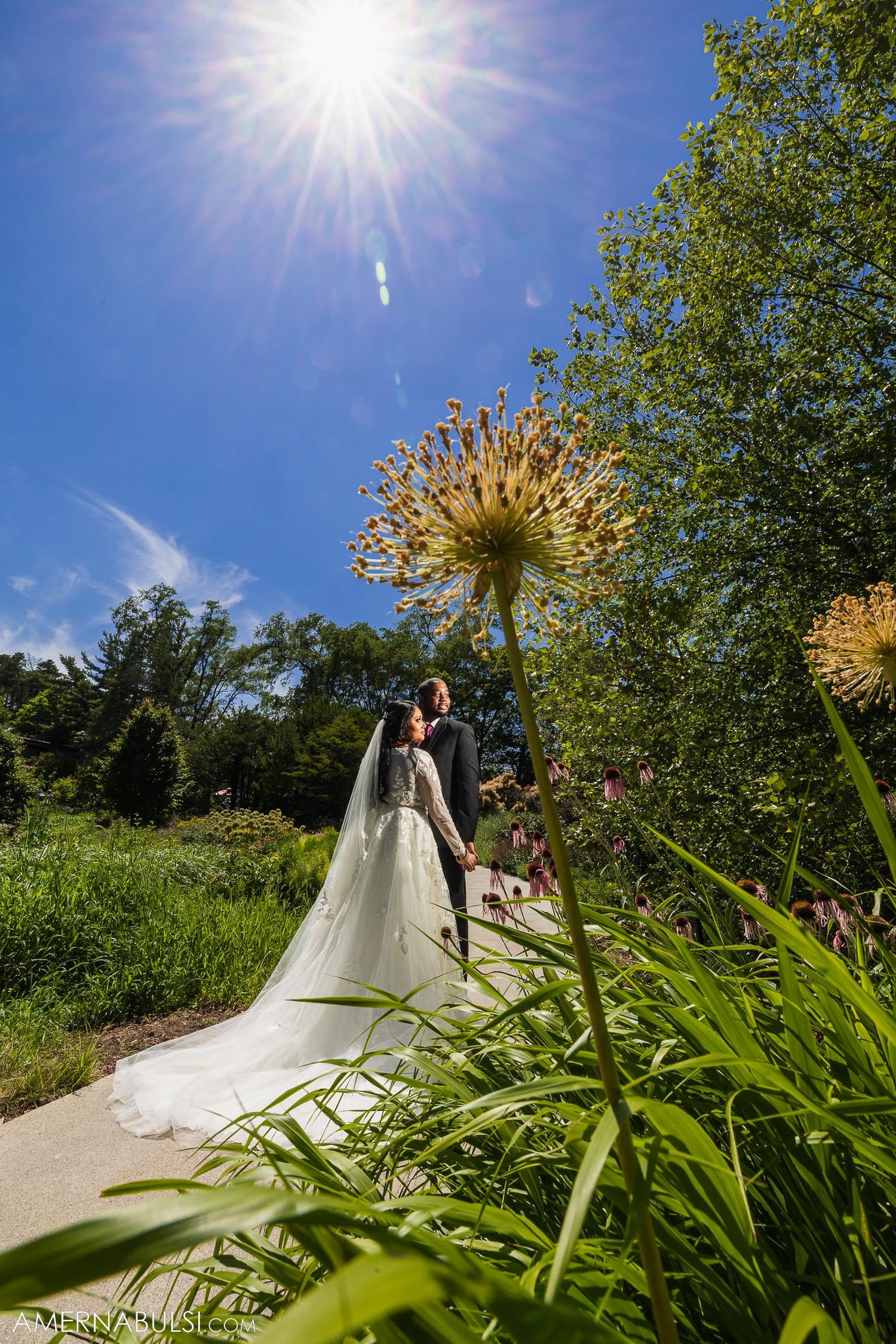 Creative wide-angle wedding photo with giant allium flower and bright sunshine.