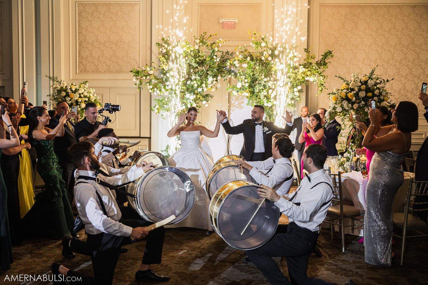Wedding celebration with drummers performing amidst floral decor and uplighting.