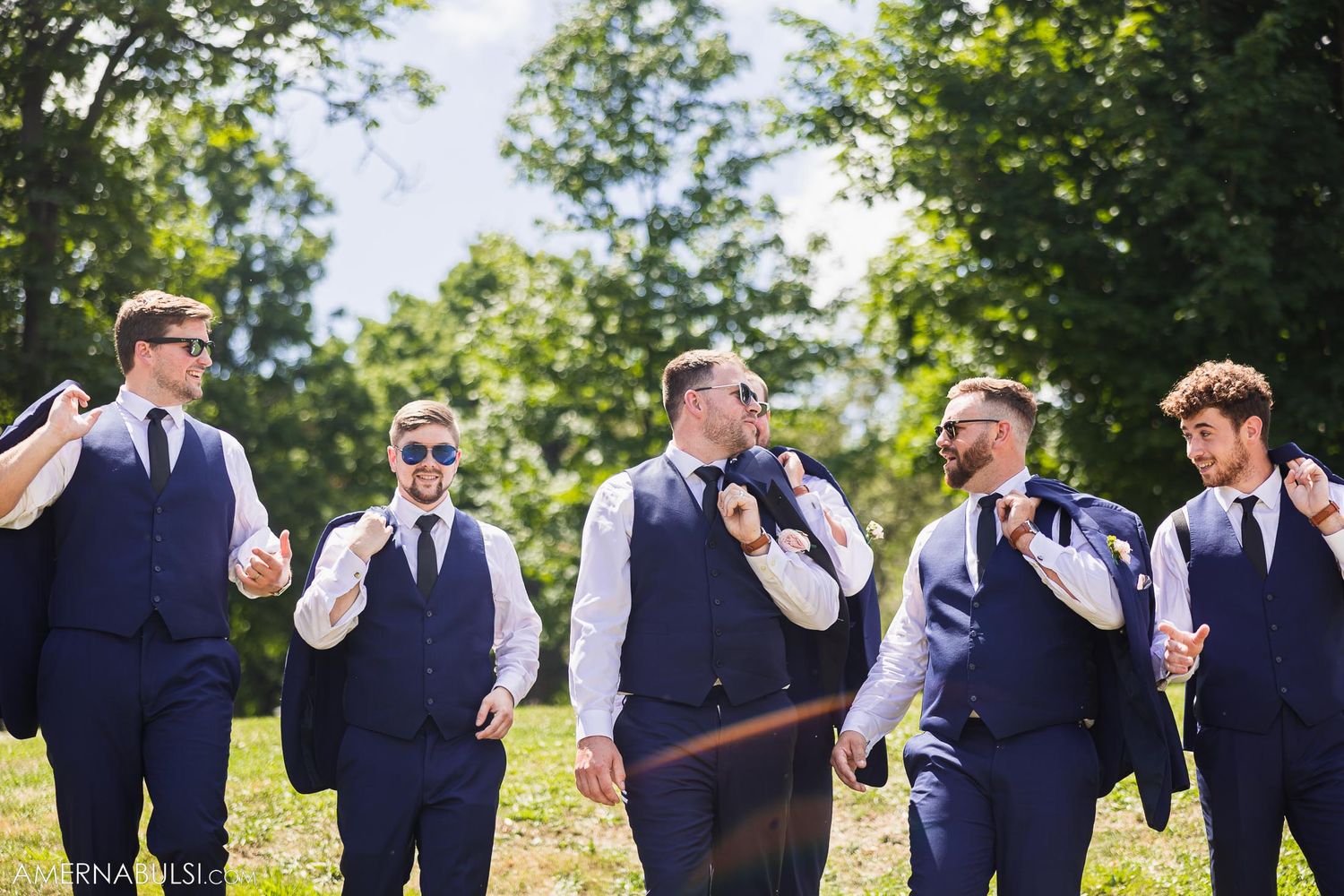 Group of groomsmen in navy attire laughing together outdoors.