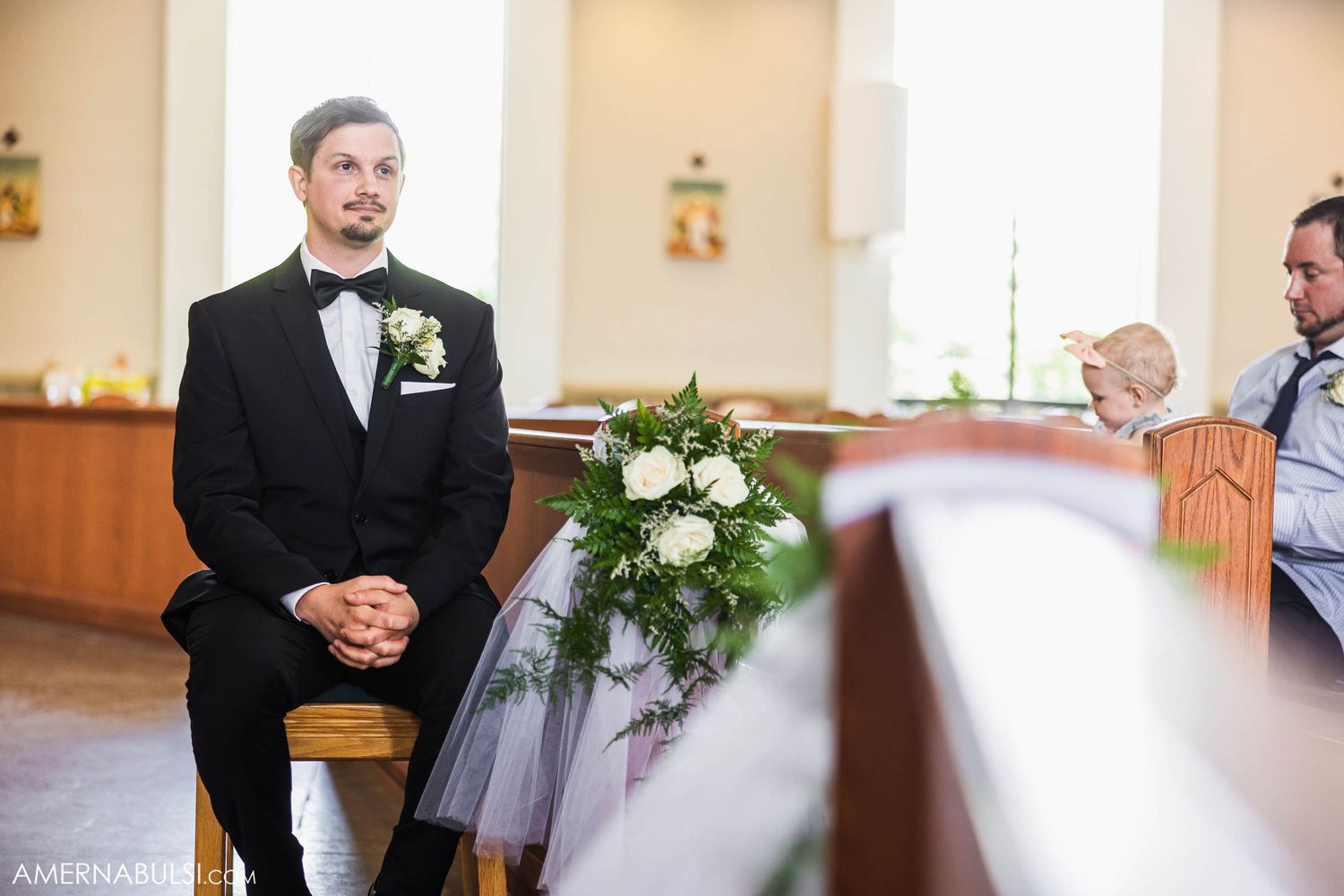 Church interior during wedding ceremony with floral decorations on wooden pews.