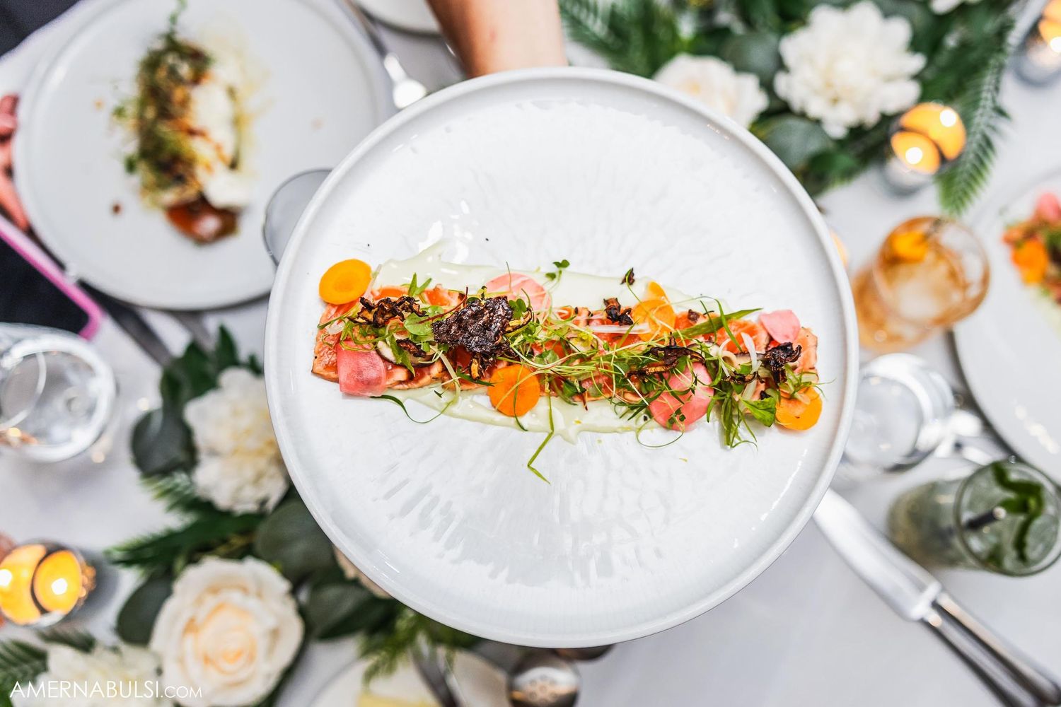Artfully plated appetizer with colorful garnishes on white plate surrounded by floral decorations.