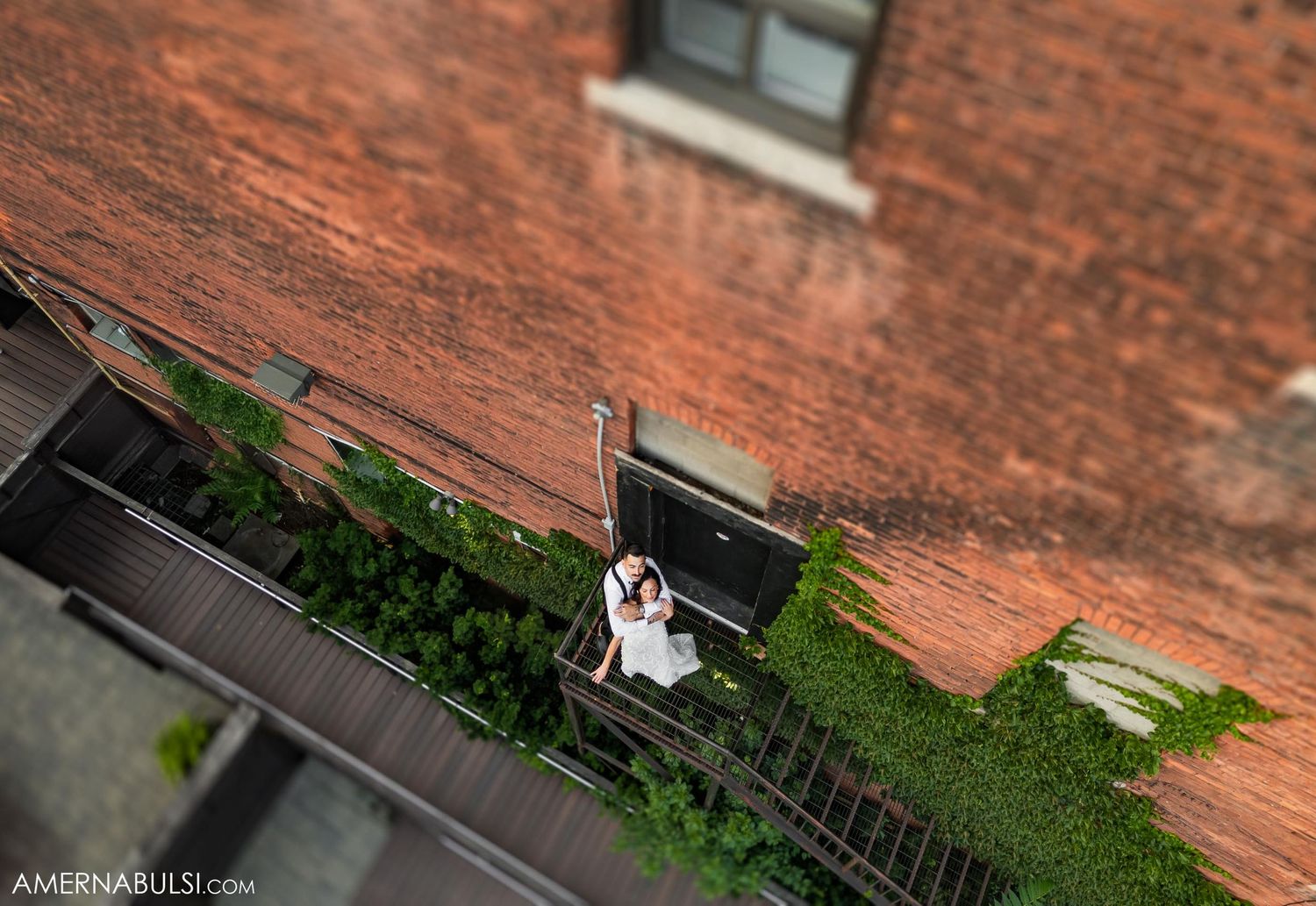 Aerial view of couple in formal attire on fire escape of brick building.
