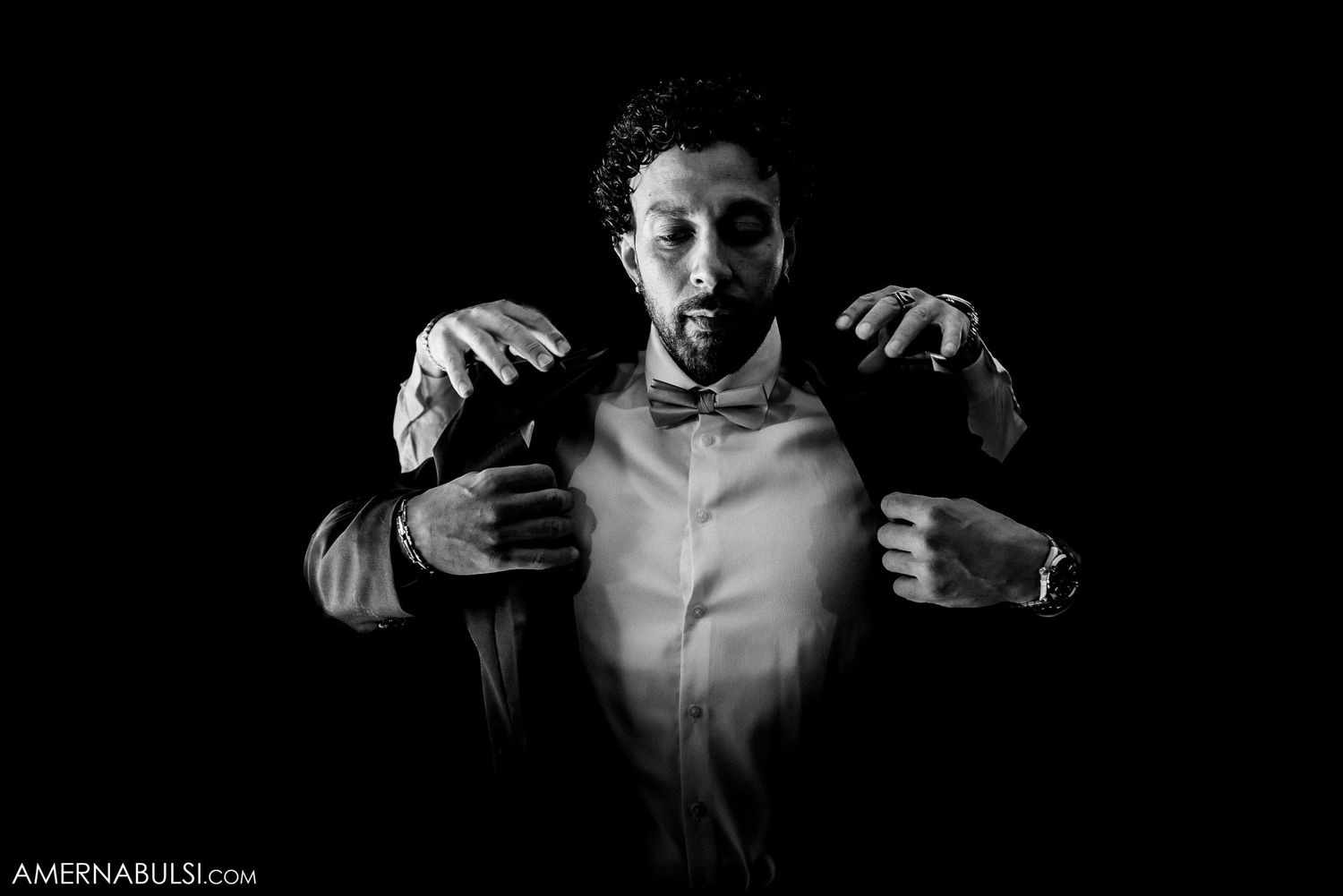 Dramatic black and white portrait of someone adjusting their bow tie in shadows.