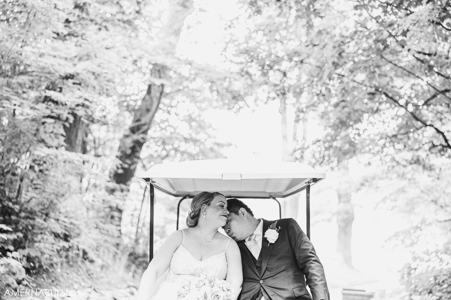 A wedding couple sharing an intimate moment while riding in a golf cart through a wooded area.