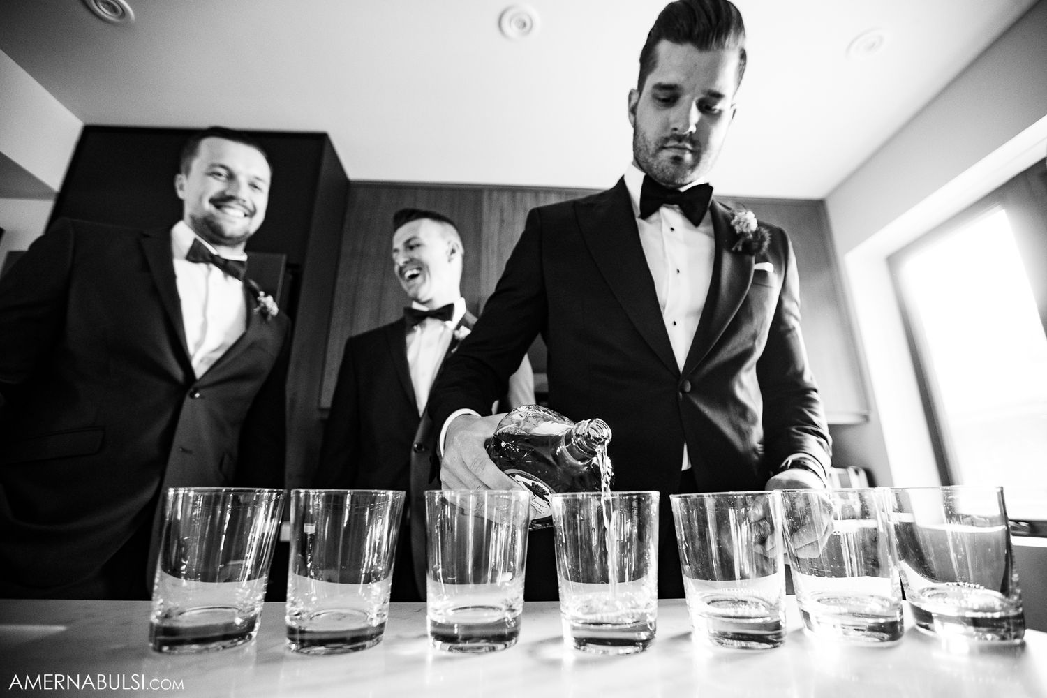 Row of whiskey glasses lined up on reflective surface in dramatic lighting.
