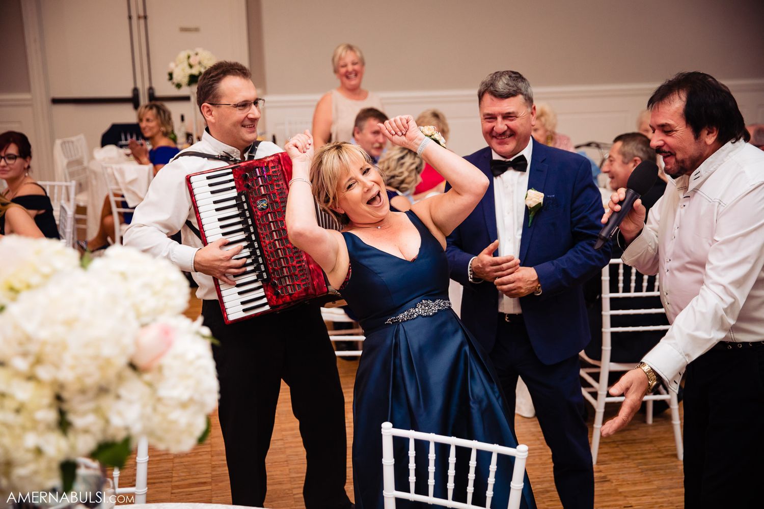 Wedding guests dance and celebrate with accordion music at an elegant indoor reception venue.