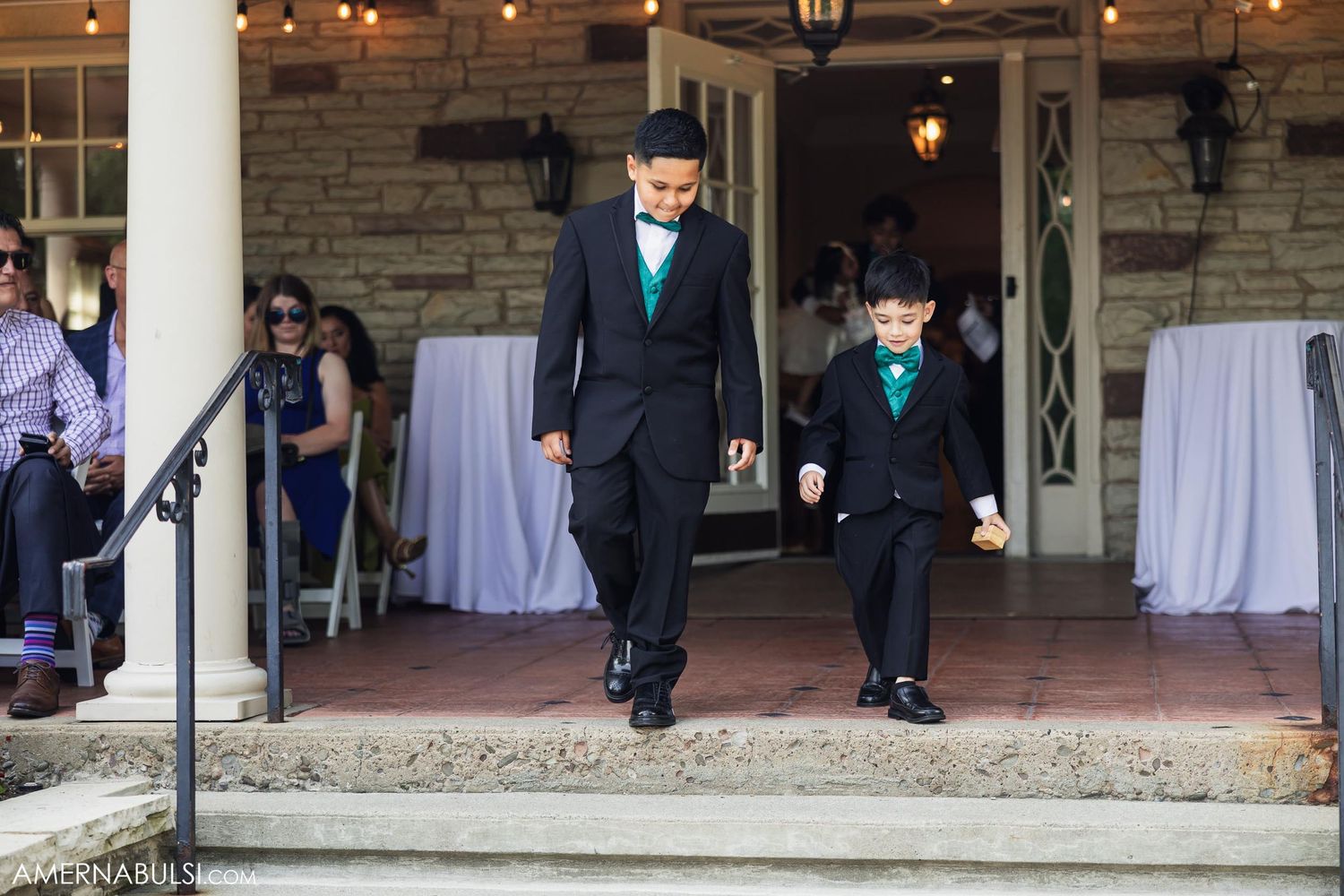 Two matching figures in black suits with teal accents descend stone venue steps.