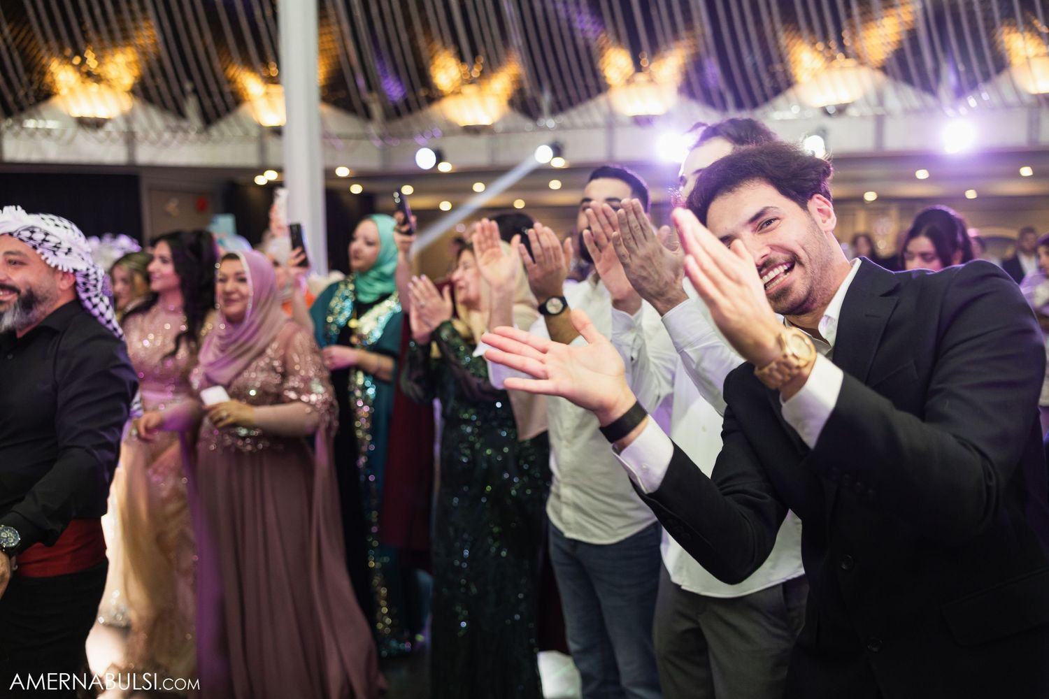 Wedding celebration showing guests dancing and clapping in a joyful group formation.