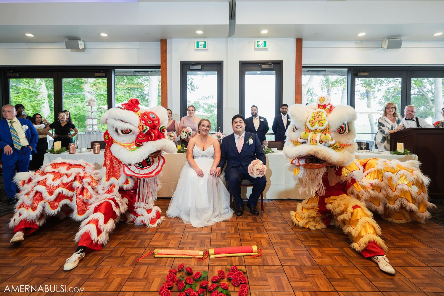 Red and gold lion dancers perform traditional ceremony for seated bride and groom.
