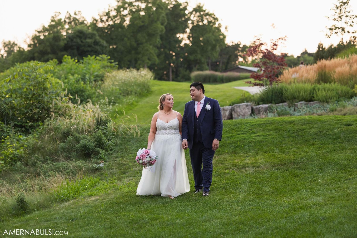 A couple walking together on a scenic grassy hill during their wedding day.