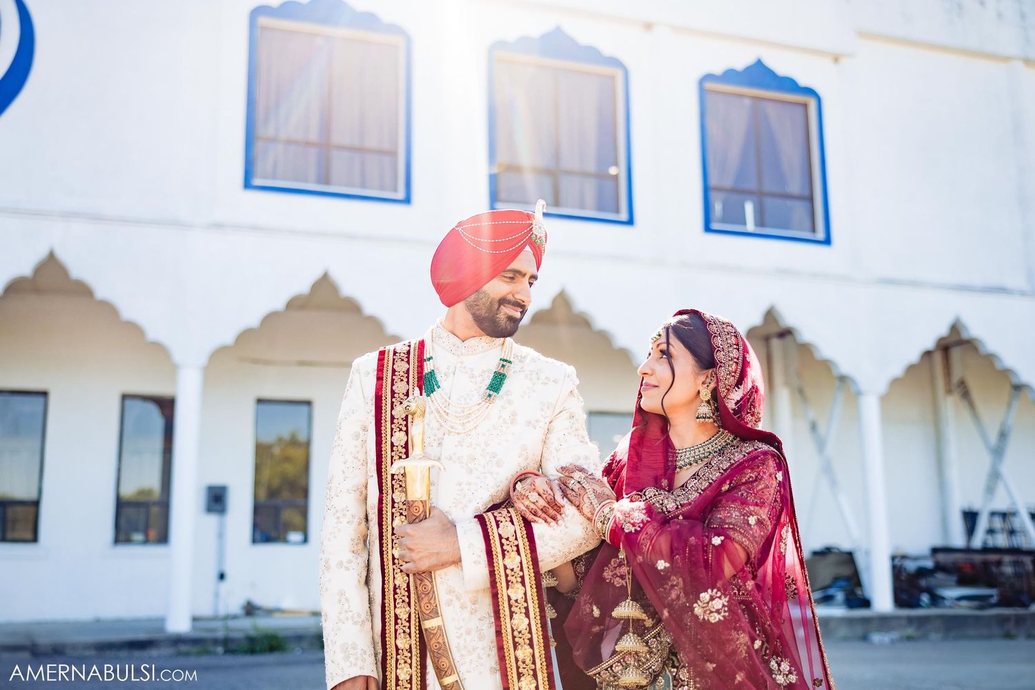 Traditional Sikh wedding couple posing outside white temple with scalloped arches.