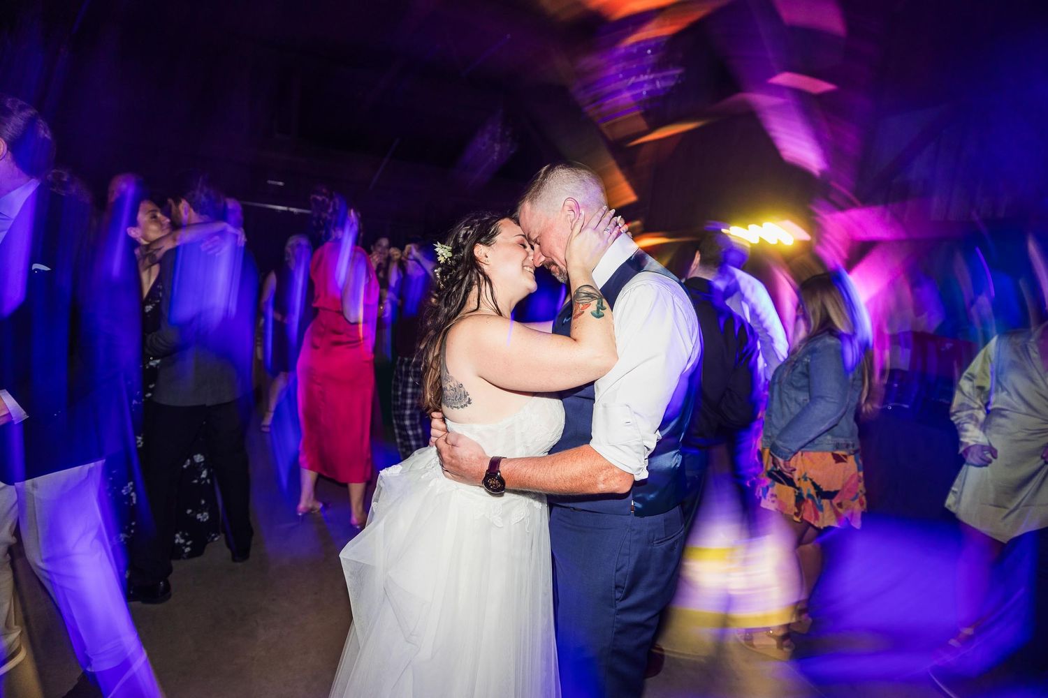 Couple dancing at wedding reception under dramatic purple lighting.
