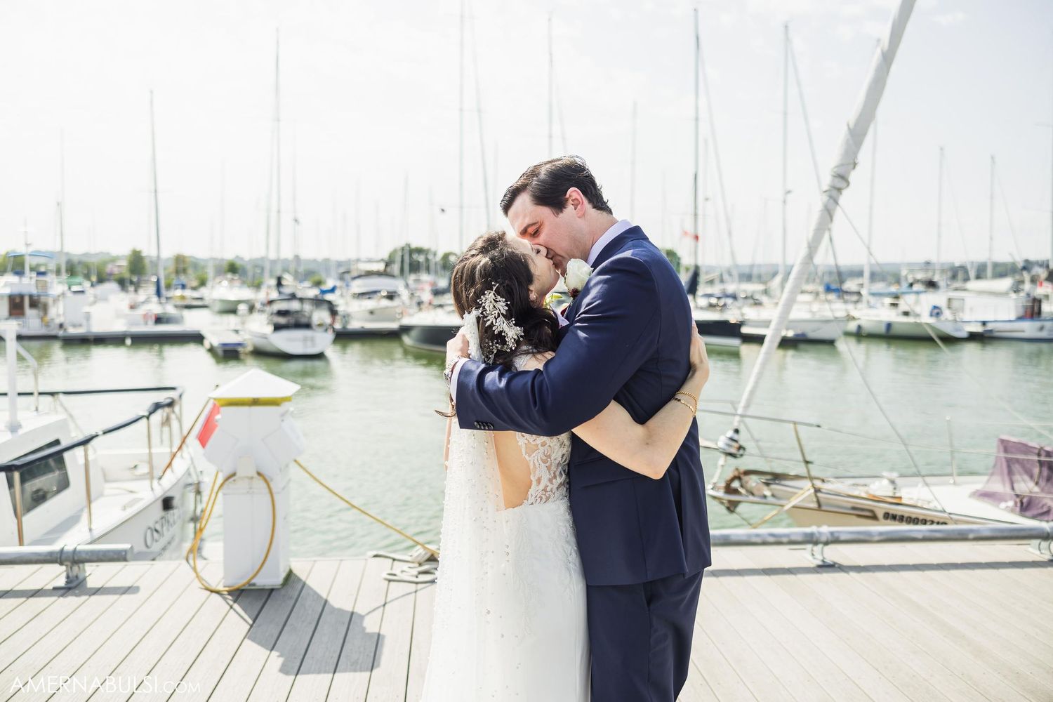 A tender embrace between newlyweds on a marina dock with sailboats in the background.